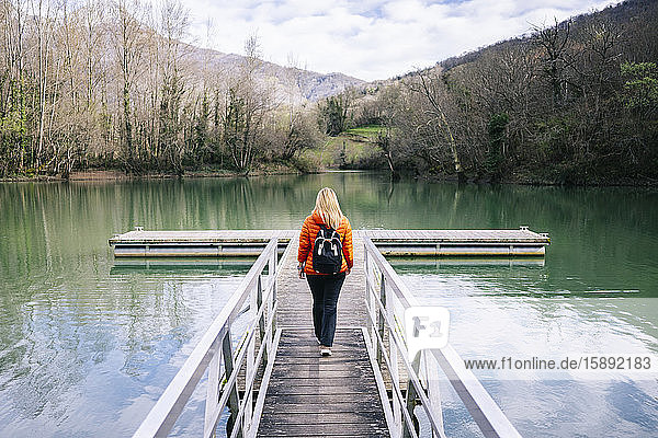 Back view of woman with backpack walking on boardwalk  Valdemurio Reservoir  Asturias  Spain