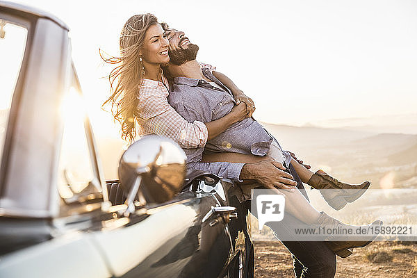 Happy affectionate couple at convertible car in the countryside at sunset