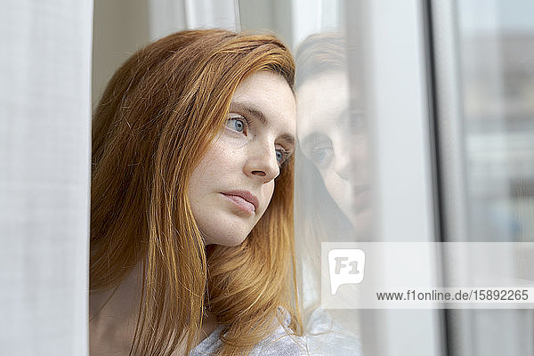 Porträt einer seriösen jungen Frau  die aus dem Fenster schaut