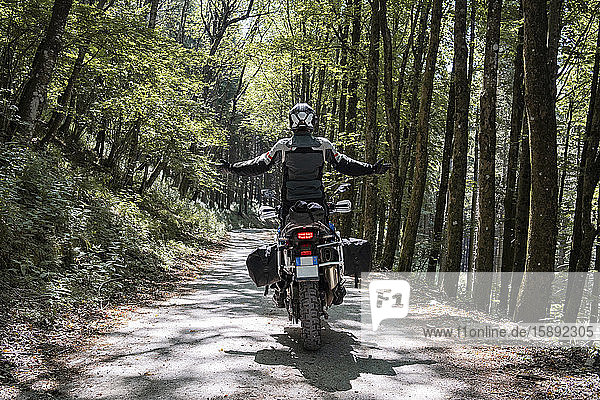 Motorradfahrer auf einer Fahrt auf einem Waldweg mit ausgestreckten Armen