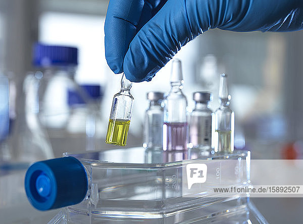 Hand of person wearing protective glove picking up pharmaceutical vial in laboratory