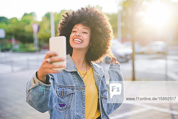 Glückliche junge Frau mit Afro-Frisur  die in der Stadt ein Selfie macht
