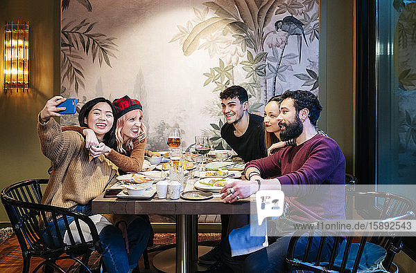 Freunde essen in einem schicken Restaurant zu Abend und nehmen sich selbst ein Smartphone