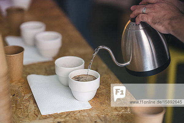 Nahaufnahme eines Mannes  der in einer Kaffeerösterei arbeitet und heißes Wasser in Kaffeetassen gießt