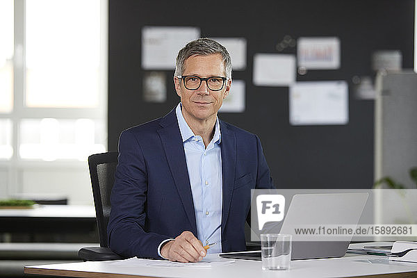 Porträt eines Geschäftsmannes mit Laptop am Schreibtisch im Büro