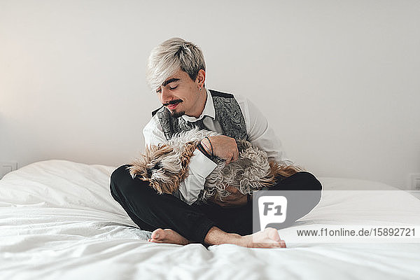 Junger Bräutigam auf dem Bett sitzend  im Schneidersitz  seinen Hund kuschelnd