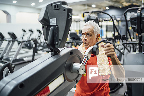 Senior man practising at exercise machine in gym