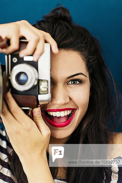 Portrait of young woman with red lips taking picture of viewer with camera