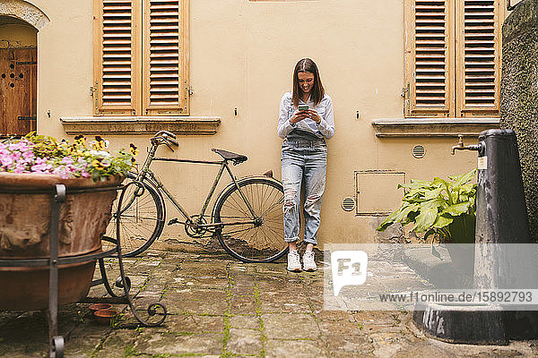 Smiling young woman standing at a house using smartphone  Greve in Chianti  Tuscany  Italy
