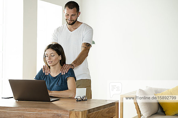 Frau arbeitet am Laptop  während ihr Freund ihr zu Hause den Nacken massiert