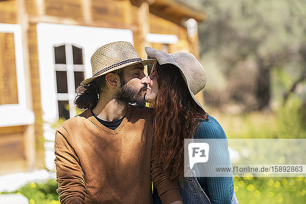 Junges Paar küsst sich vor einer Holzhütte