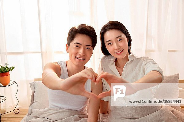 Happy young couple in bed do heart-shaped gestures
