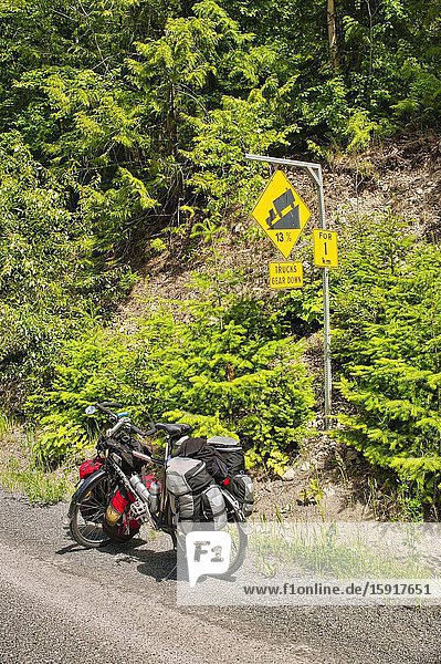 Loaded bicycle beside steep downhill warning sigh Duffy Lake Road Cayoosh Mountain Range British Columbia Canada.