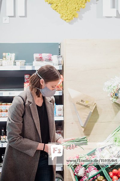Woman in mask buying vegetables at grocery store.