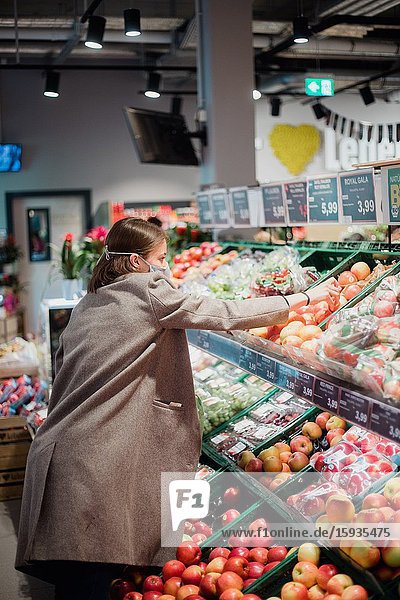 Woman in mask buying fruits at grocery store.