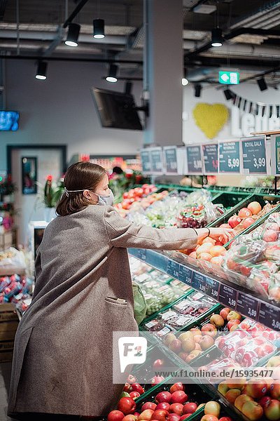 Woman in mask buying fruits at grocery store.