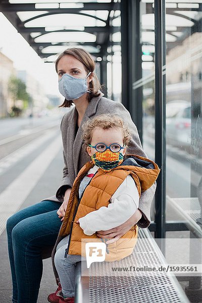 Mother and son with mask waiting for the bus.