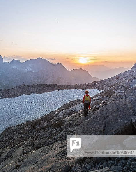 Hiker stands in rocky alpine terrain and looks at sunset over Gosaukamm with mountain peak Bischofsmütze  evening mood  Salzkammergut  Upper Austria  Austria  Europe
