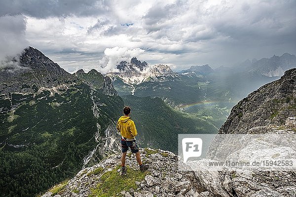 Young man  in the back mountain peak Monte Cristallo with rainbow  hiker in the mountains  via ferrata Vandelli  Sorapiss circuit  Dolomites  Belluno  Italy  Europe