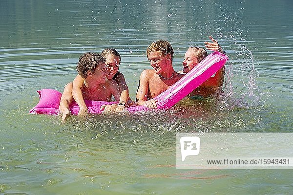 Vier Teenager auf einer Luftmatraze im Wasser haben Spaß beim Baden  18 Jahre  Mondsee  Oberösterreich  Österreich  Europa
