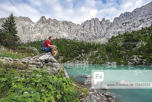 Wanderer sitzt  rastet auf einem Fels an türkisgrünem Sorapissee  Lago di Sorapis  Dolomiten  Belluno  Italien  Europa