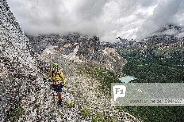 Junger Mann  Bergsteiger an einem Klettersteig  Via Ferrata Vandelli  Blick auf Lago di Sorapis  Sorapiss Umrundung  Berge mit tiefhängenden Wolken  Dolomiten  Belluno  Italien  Europa