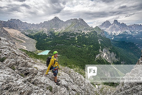 Young man  hiker on a fixed rope route  Via Ferrata Vandelli  view of Lago di Sorapis and the peaks of Cime de Laudo and Monte Cristallo  Sorapiss circuit  mountains with low clouds  Dolomites  Belluno  Italy  Europe