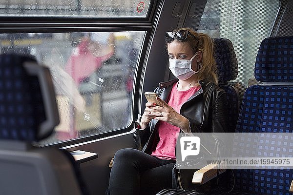 Frau mit Mundschutzmaske  sitzt in Zug  am Handy  Corona-Krise  Stuttgart  Baden-Württemberg  Deutschland  Europa