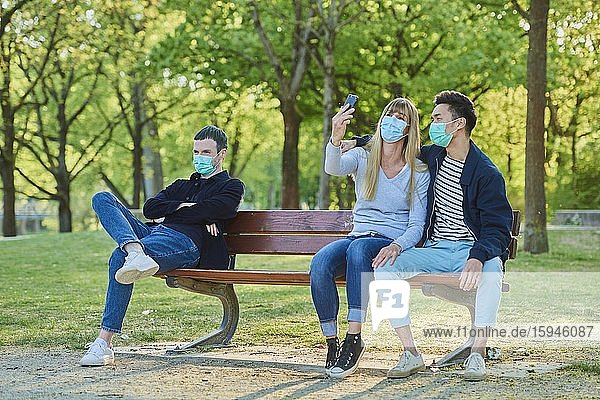Ein Mann und ein Paar mit Mundschutzmaske auf einer Parkbank in einem Stadtpark  Corona-Krise  Regensburg  Bayern  Deutschland  Europa