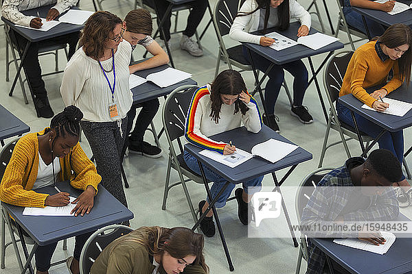 Gymnasiallehrer beaufsichtigt Schüler  die an Tischen Prüfungen ablegen