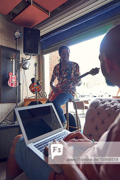 Musicians with laptop and electric guitar in garage recording studio