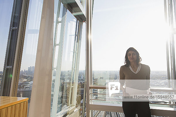 Porträt einer selbstbewussten Geschäftsfrau am Fenster eines sonnigen Hochhausbüros