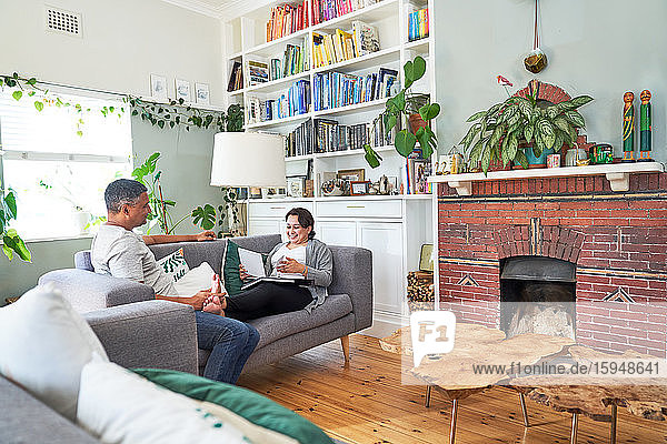 Ein erwachsenes Paar liest und spricht auf dem Wohnzimmersofa