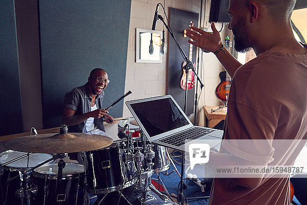Happy musicians with drums and laptop in recording studio