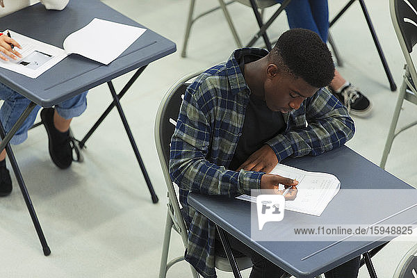 Focused high school boy student taking exam at desk in classroom