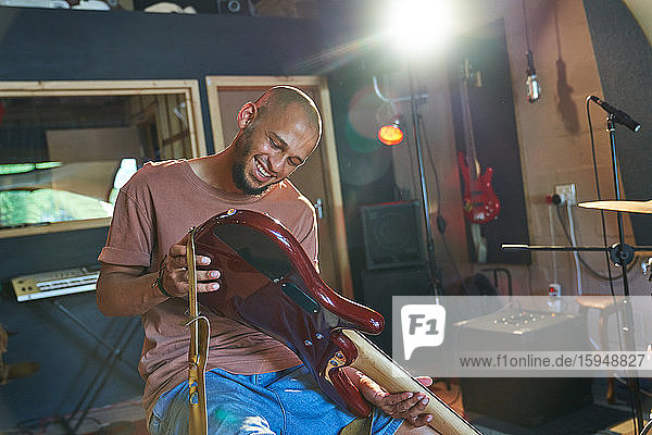 Lächelnder männlicher Musiker inspiziert Gitarre im Aufnahmestudio