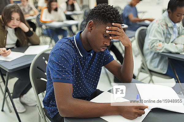 Fokussierter High-School-Junge nimmt Prüfung am Schreibtisch im Klassenzimmer ab