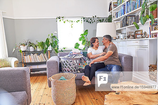 Affectionate mature couple doing laundry on living room sofa