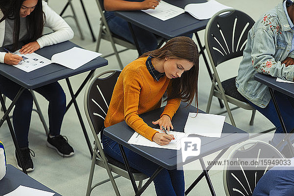 Focused high school girl student taking exam at desk in classroom