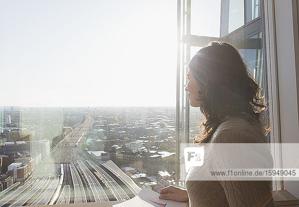Nachdenkliche Geschäftsfrau am sonnigen Fenster mit Blick auf die Stadt