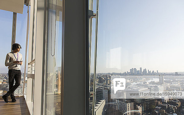 Businessman standing at sunny urban highrise office window