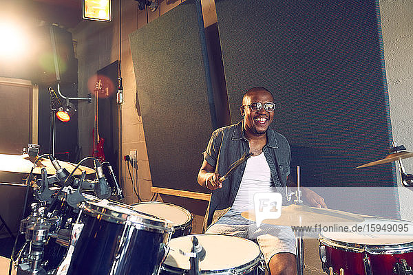 Glücklicher männlicher Musiker spielt Schlagzeug im Aufnahmestudio