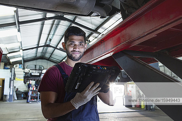 Portrait confident male mechanic with diagnostic equipment in auto repair shop