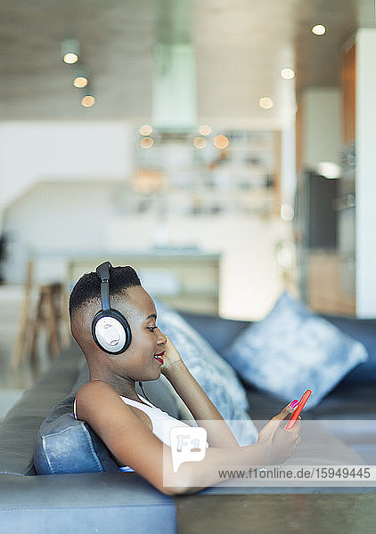 Young woman listening to music with headphones and mp3 player on sofa