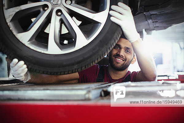 Porträt eines selbstbewussten  lächelnden Mechanikers  der in einer Autowerkstatt unter dem Auto arbeitet