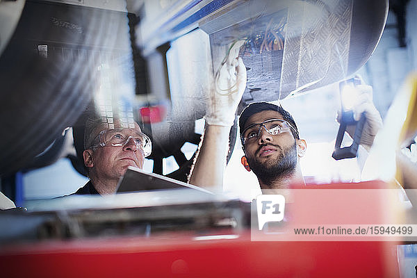 Männliche Mechaniker arbeiten unter dem Auto in einer Autowerkstatt