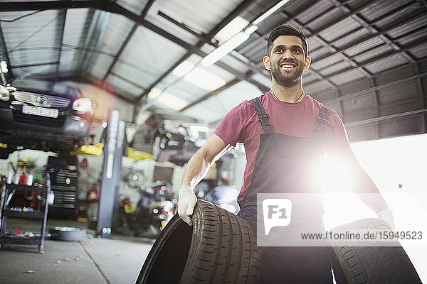Porträt eines lächelnden männlichen Mechanikers mit Reifen in einer Autowerkstatt