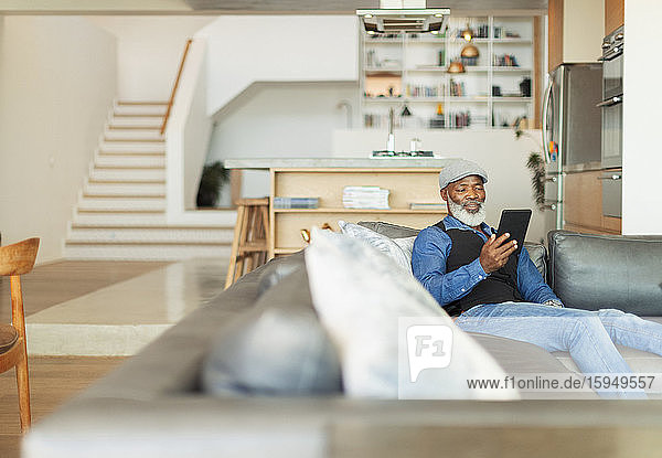 Mann benutzt digitales Tablett auf Wohnzimmer-Sofa