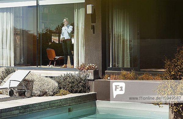 Businessman talking on smart phone at sunny  modern patio window