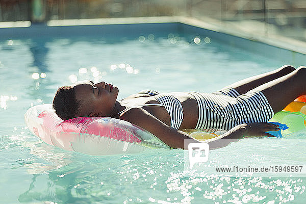 Gelassene junge Frau liegt auf einem aufblasbaren Floß im sonnigen Schwimmbad